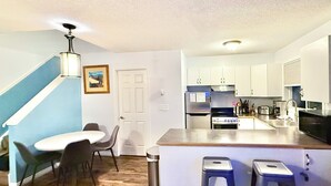 A compact kitchen with a central island, a dining area with chairs, and a staircase. - Mountain View Cozy 2-Storey Chalet, 2 BR , 1.5 BTH, Hot Tub, BBQ (Harvie Heights)