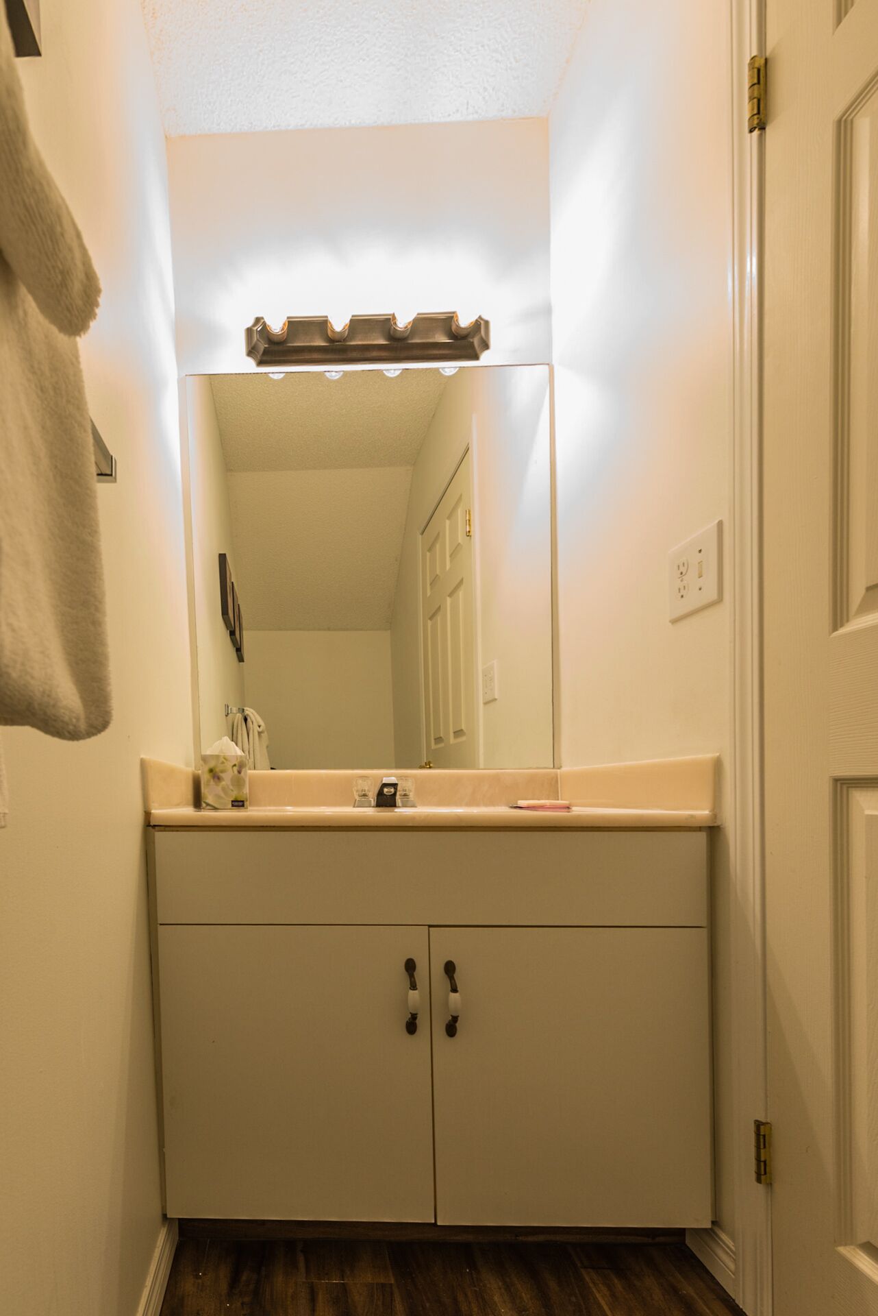 A bathroom with a white vanity, a mirror, and a towel hanging on the wall.