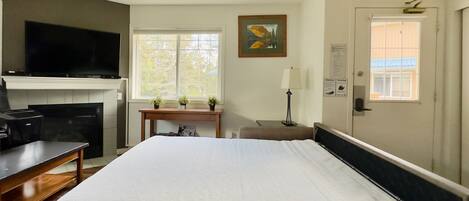 A hotel room with a bed, a TV, a desk, a chair, a window, and a door.