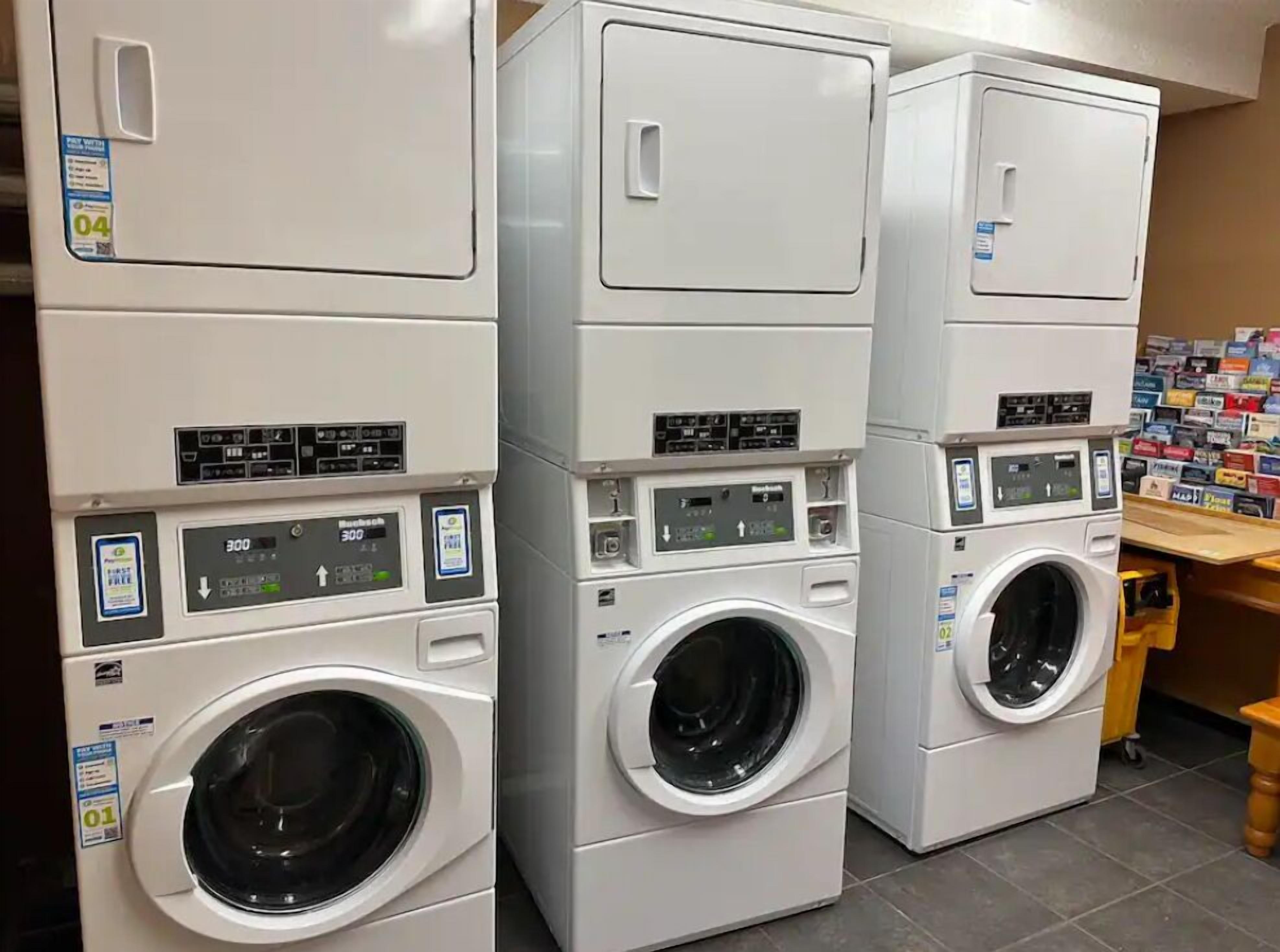 A laundromat with stacked front-loading washers and dryers, control panels, and a wall of laundry supplies.