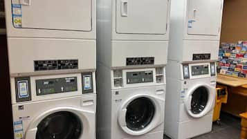 A laundromat with stacked front-loading washers and dryers, control panels, and a wall of laundry supplies.