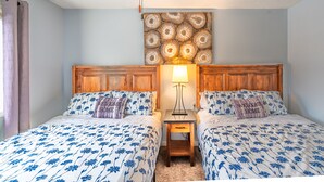 A hotel room with two beds, a wooden headboard, a nightstand with a lamp, and a wall art piece above the beds. - Mountain View Cozy 2-Storey Chalet, 2 BR , 1.5 BTH, Hot Tub, BBQ (Harvie Heights)