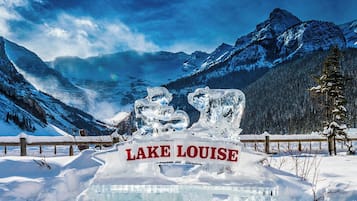 An ice sculpture with 'LAKE LOUISE' text in the foreground, surrounded by snow-covered mountains and trees.