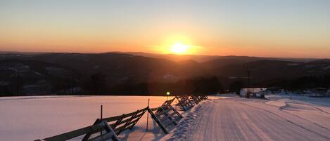 A snow-covered road with a wooden fence on one side and a sunset in the background.
