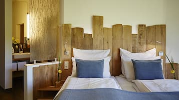 A bedroom with a wooden headboard, two beds with white linens and blue pillows, a wooden nightstand, and a bathroom with a sink and mirror.
