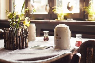 Una mesa con una taza blanca que dice "VETTINS", un vaso de líquido rojo y un macetero de madera con plantas verdes.