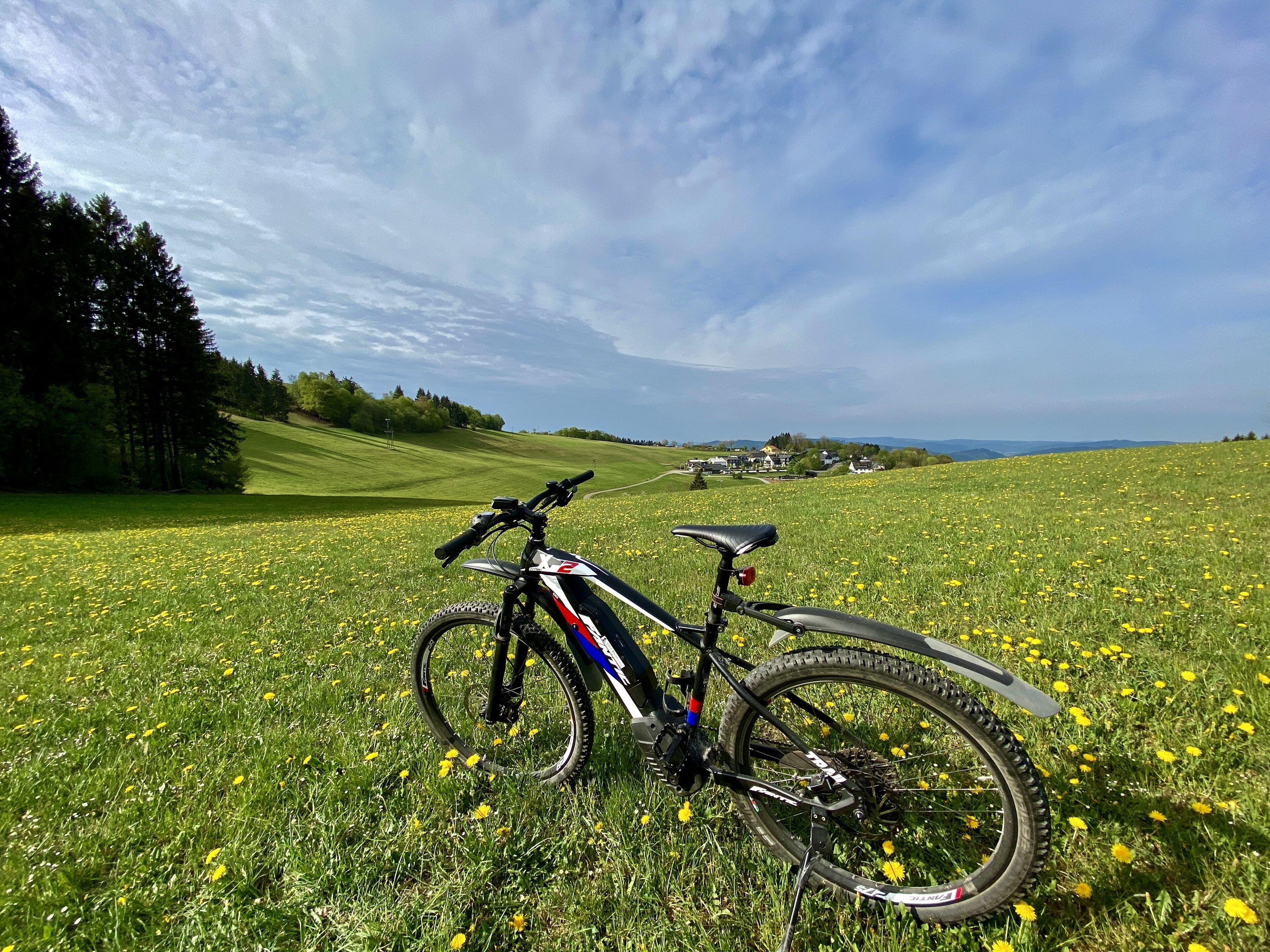 Una bicicleta de montaña estacionada en un campo cubierto de césped, con cielo despejado y casas a la distancia.