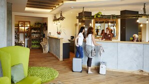 Zona de recepción con un mostrador de madera, un sillón verde y un pequeño rincón de estar con alfombra verde.