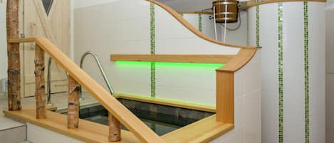 Un baño moderno con una bañera de madera, cabina de ducha de vidrio y una pared iluminada en verde.