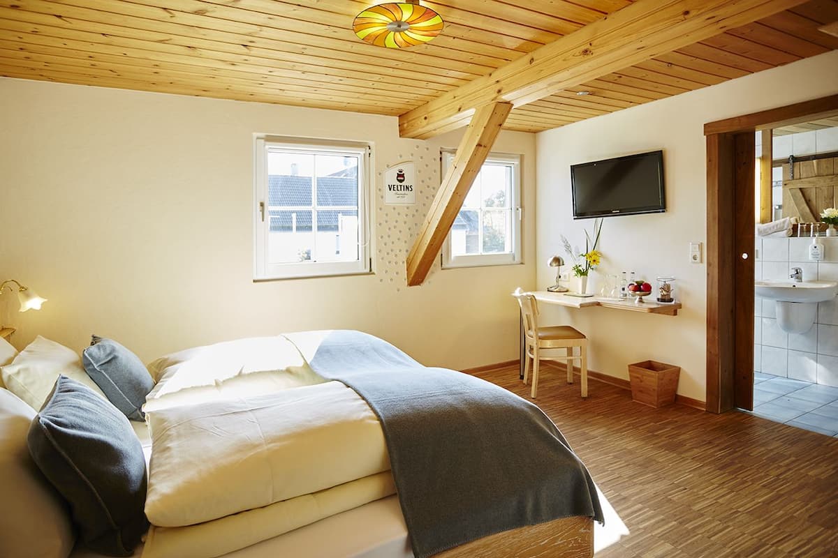 A bedroom with a bed, a desk, a chair, a TV, and a bathroom visible through an open door.