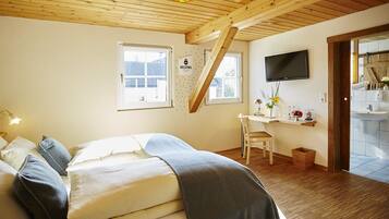 A bedroom with a bed, a desk, a chair, a TV, and a bathroom visible through an open door.