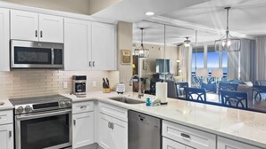 Una cocina moderna con armarios blancos, electrodomésticos de acero inoxidable y vistas a un comedor con balcón.