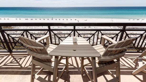 Un patio frente a la playa con una mesa y sillas, con vista a una playa de arena y un mar turquesa.