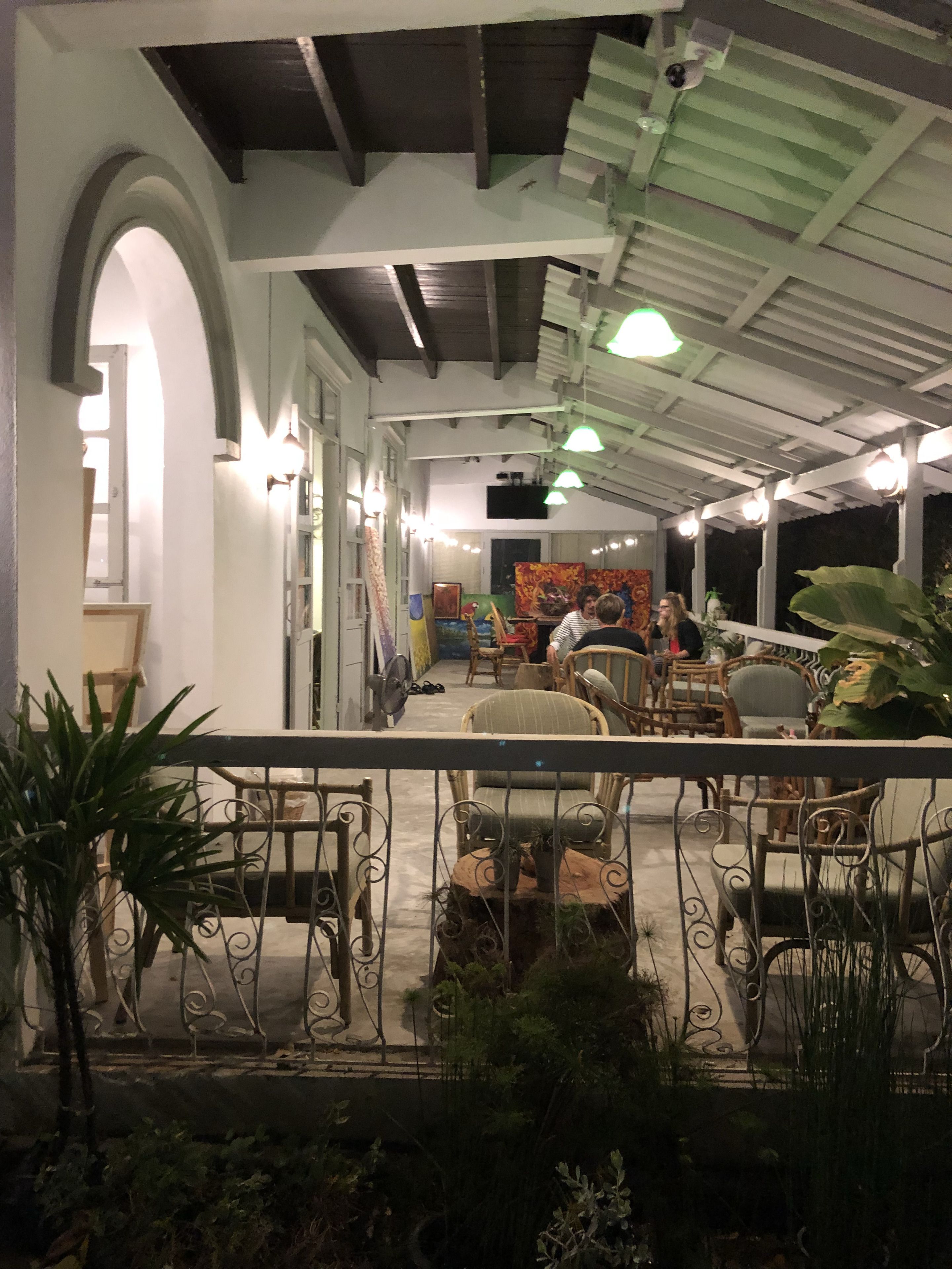 An indoor space with a high ceiling, wooden beams, and a series of hanging lights. There are several chairs and tables arranged for seating and dining.