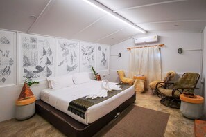 A neatly arranged bedroom with a bed, two chairs, a small table, and wall art. - Silsopa Hostel (Nong Khai)
