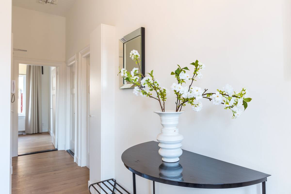 A hallway with a round table and a white vase with flowers.