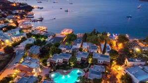 An aerial view of a coastal residential area with a swimming pool surrounded by houses, boats in the water, and a distant view of a cityscape.