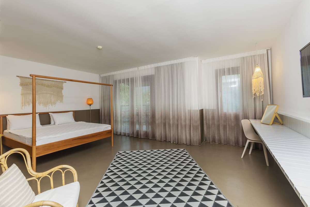 Una habitación de hotel moderna con cama con dosel, un escritorio y un ventanal con cortinas traslúcidas.