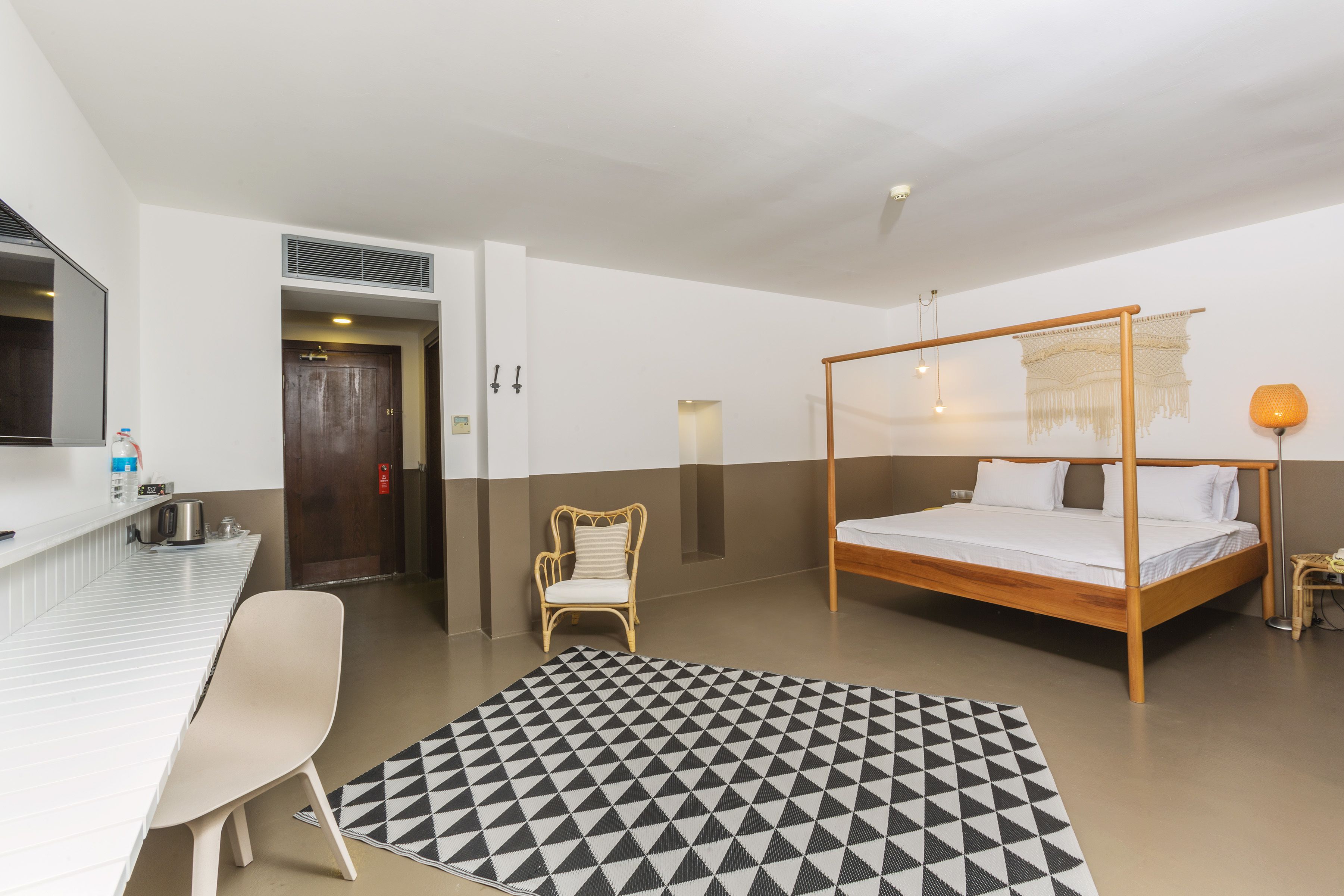 Une chambre d’hôtel avec un lit, un bureau, une chaise, une petite table et un tapis à motifs.