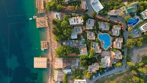 An aerial view of a coastal resort with multiple buildings, a swimming pool, and a dock with boats.