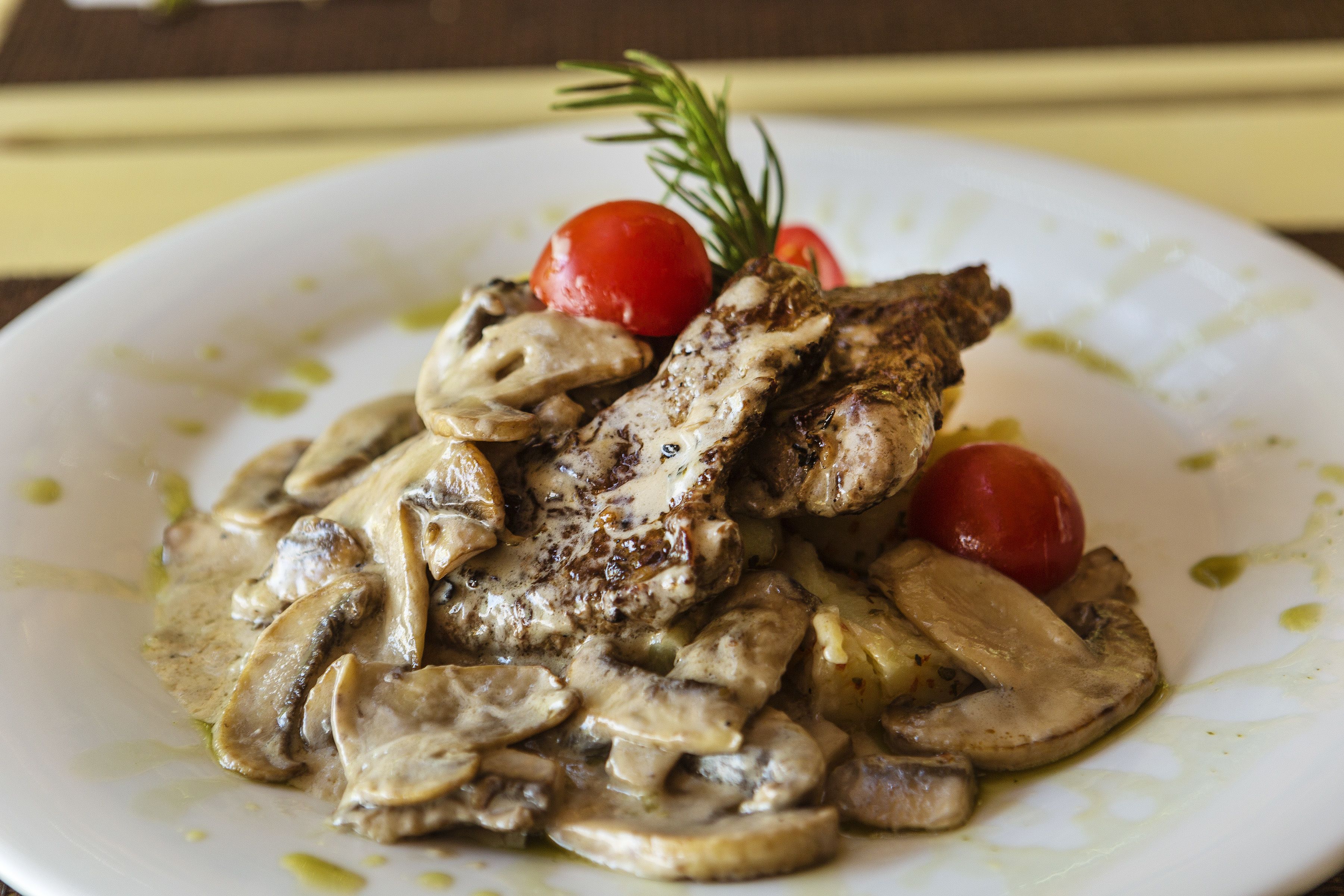 A plate of food with grilled meat, mushrooms, and cherry tomatoes, garnished with a sprig of rosemary.