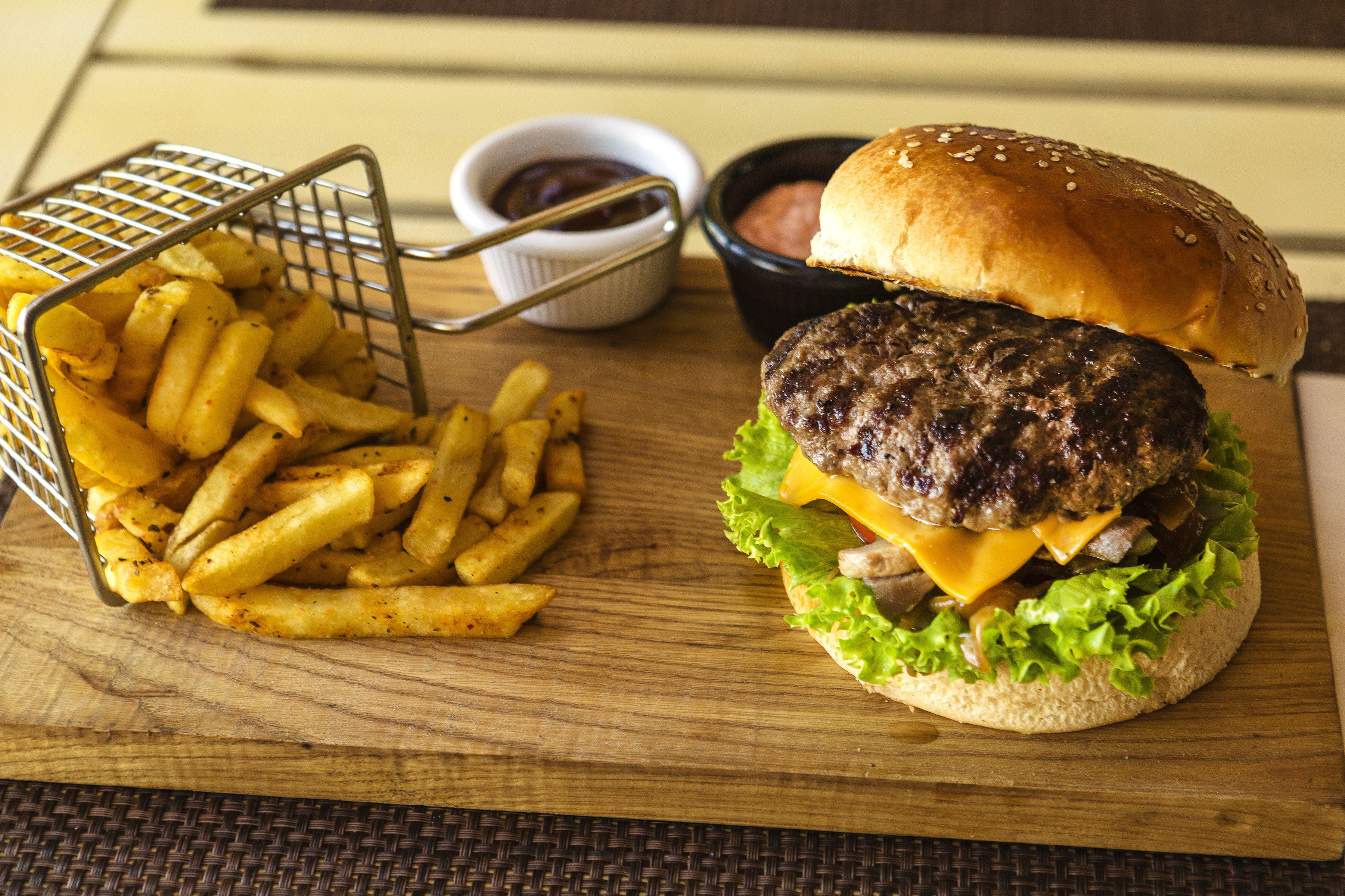 A burger with lettuce, cheese, and a bun, accompanied by a basket of fries and two small bowls of sauce.