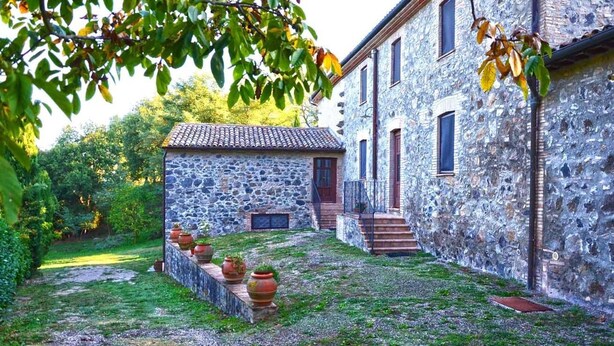 Edifici de pedra amb teulada arajolada, un petit jardí amb plantes en testos i una escala que condueix a l'entrada.