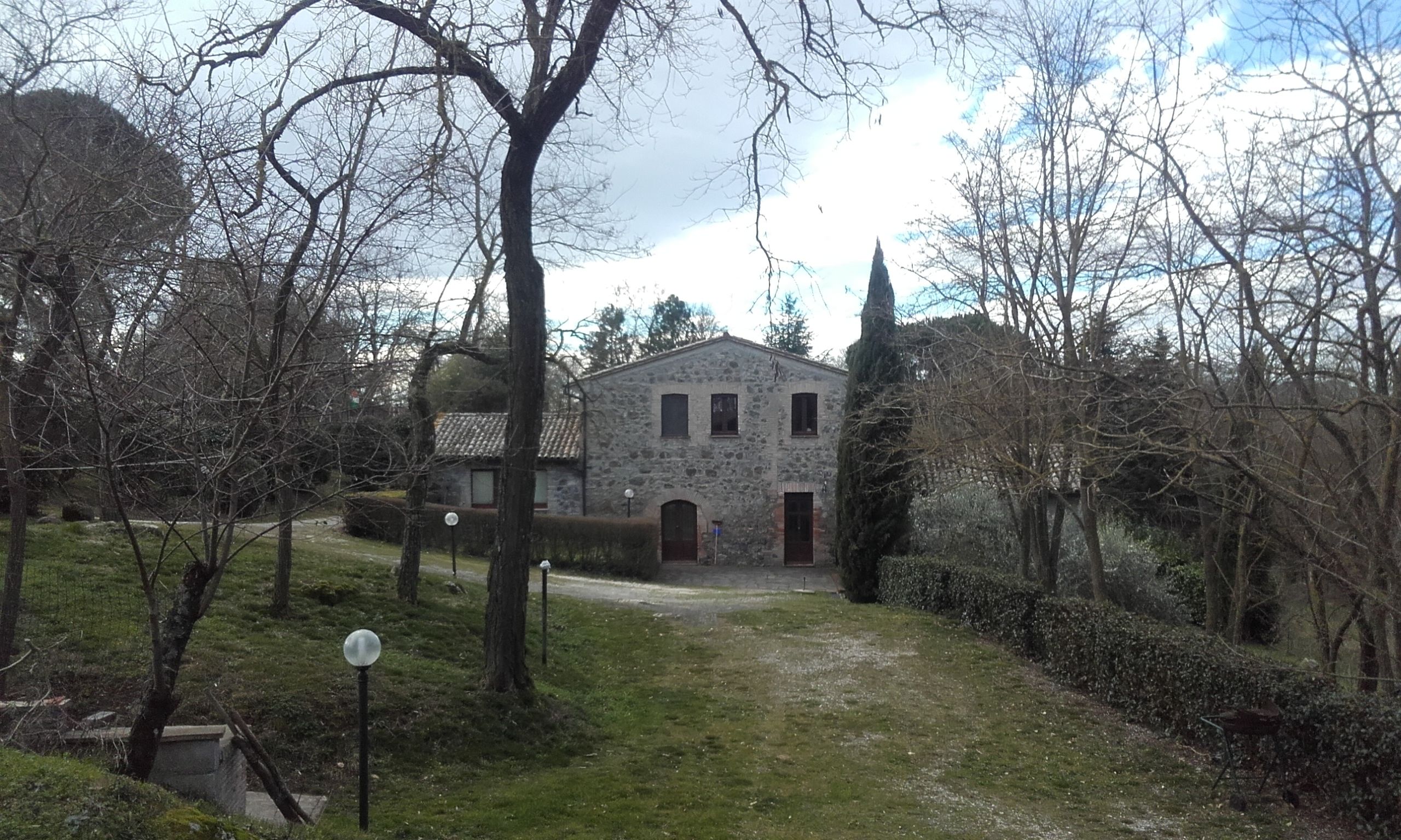 Un edificio de piedra con una entrada central, rodeado de árboles y un área verde.