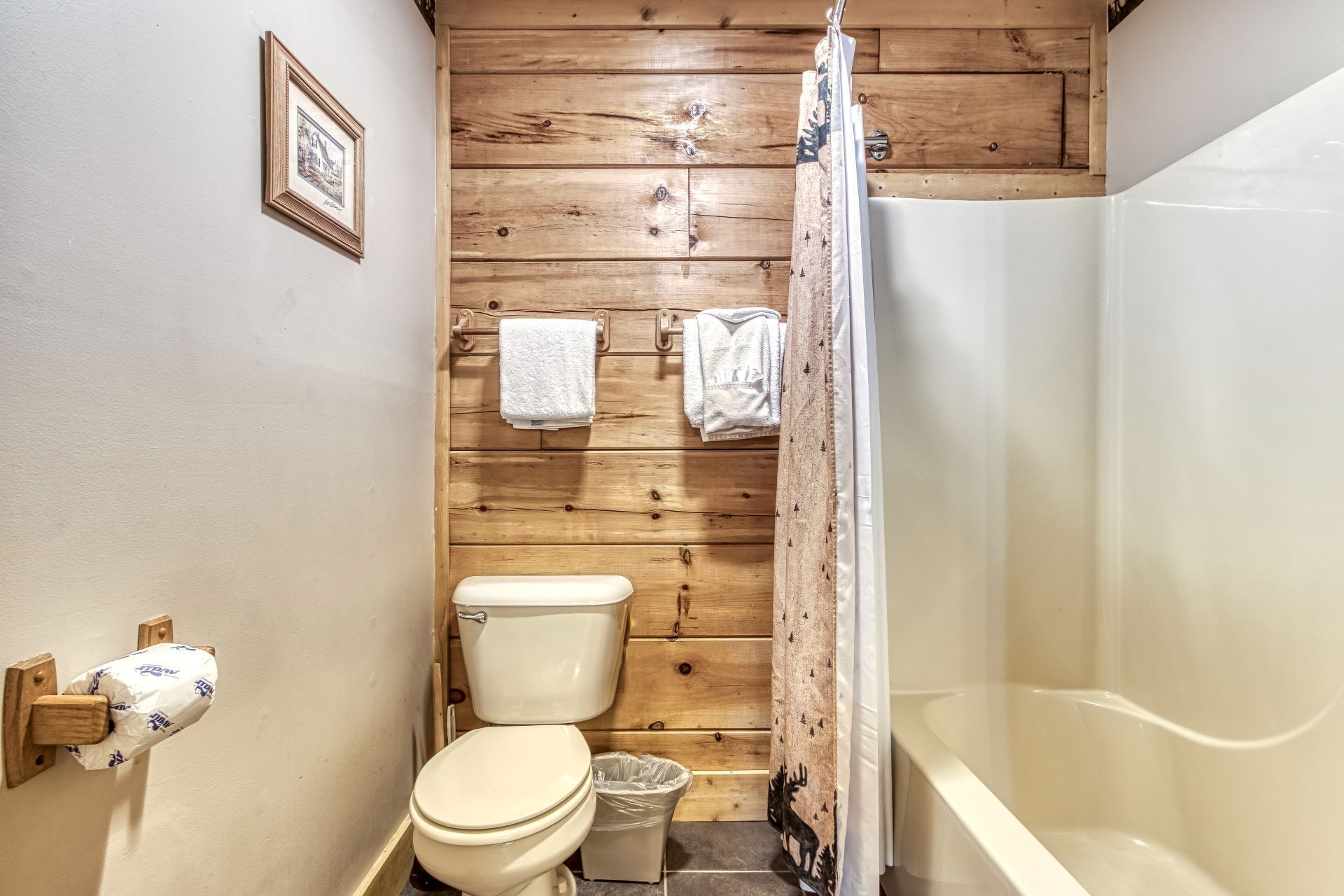 A bathroom with wooden panel walls, a toilet, a shower with a curtain, and two towels on a rack.
