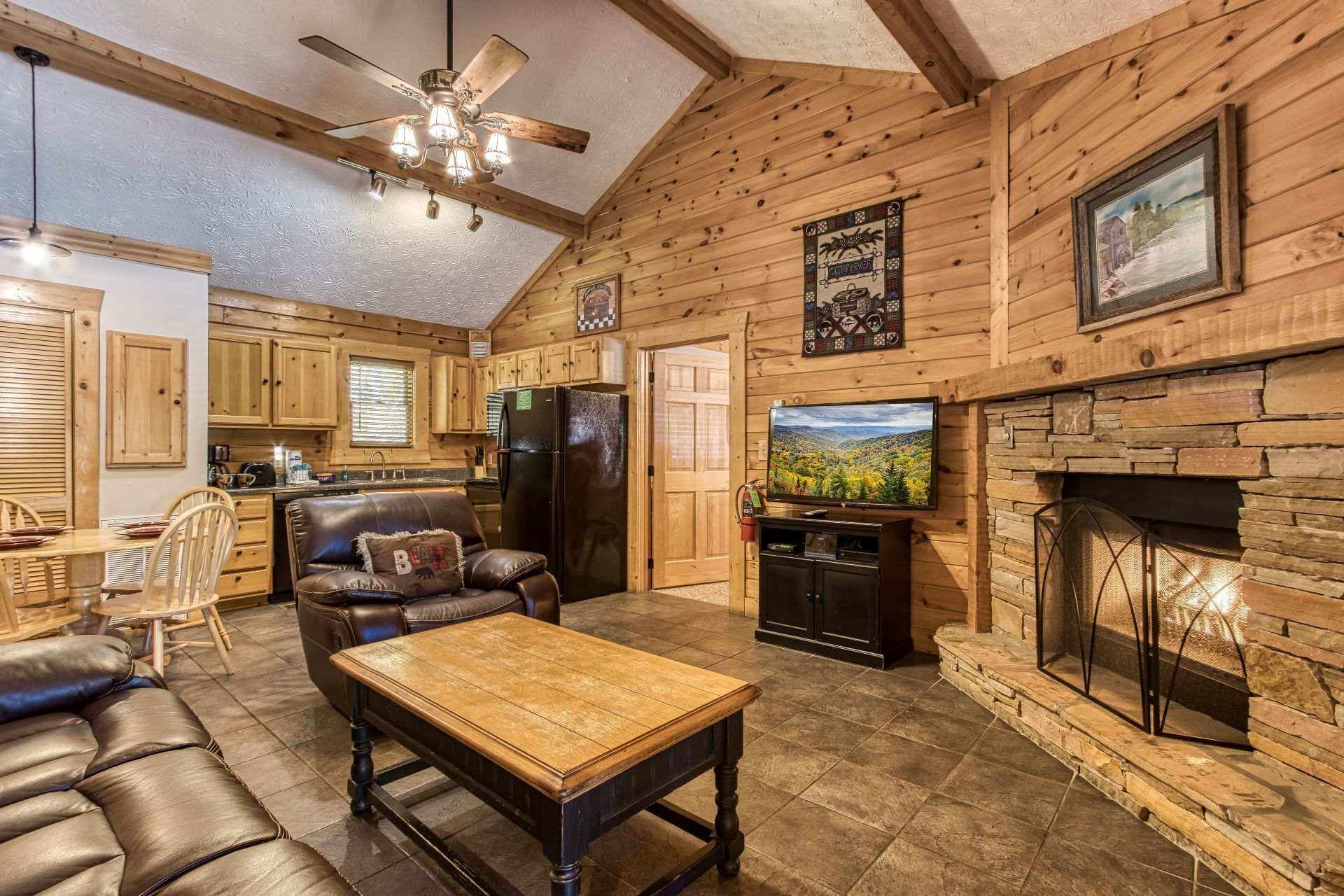 L’intérieur chaleureux d’un chalet en bois comprend une cheminée, un coin repas avec une table et des chaises en bois, un canapé en cuir et un téléviseur.