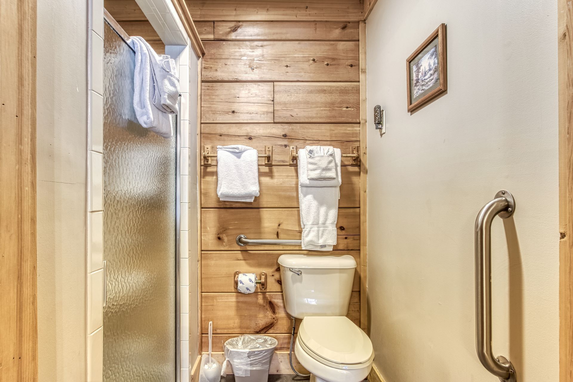 Un baño pequeño y funcional con paneles de madera, inodoro blanco, barandilla y toallero con dos toallas.
