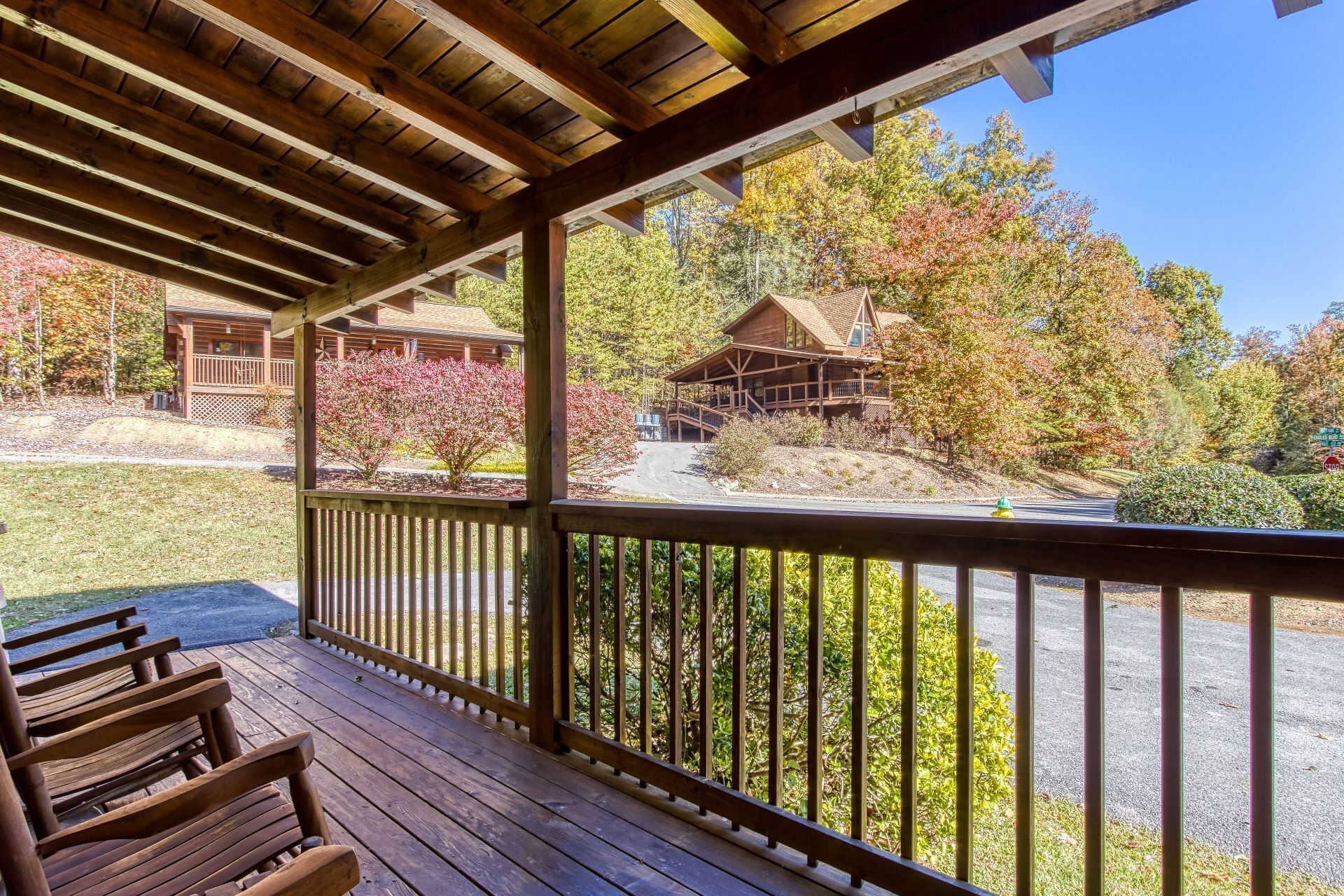 A wooden deck with benches, overlooking a forested area with autumn-colored trees and a lodge.