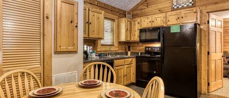 A wooden cabin interior with a dining table set for four, a black refrigerator, wooden cabinets, and a microwave.