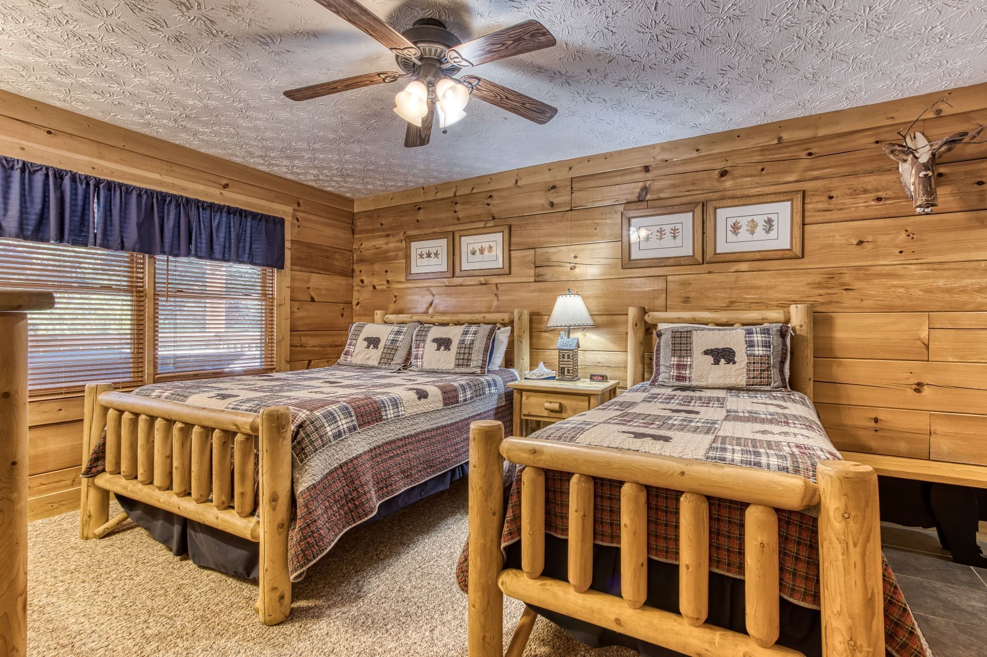 A cabin-style bedroom with two wooden beds, a ceiling fan, and a rustic decor theme.
