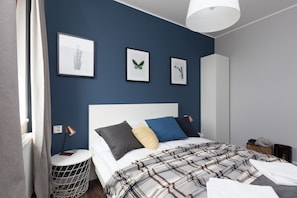A modern bedroom with a large bed, a bedside table with a lamp, and framed artwork on the wall.
