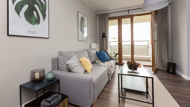 Un moderno salón con un sofá gris, una mesa de centro y un ventanal con cortinas.