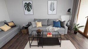 Una sala de estar moderna con un sofá gris, una mesa de centro de vidrio y una planta en maceta.