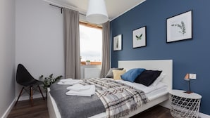 Un dormitorio moderno con cama, una silla, una mesita de noche y una ventana con cortinas.