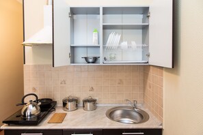 A kitchen with a stove, pots, a kettle, a sink, and a cabinet with dish racks. - Hotel Station Korolev (Korolev)