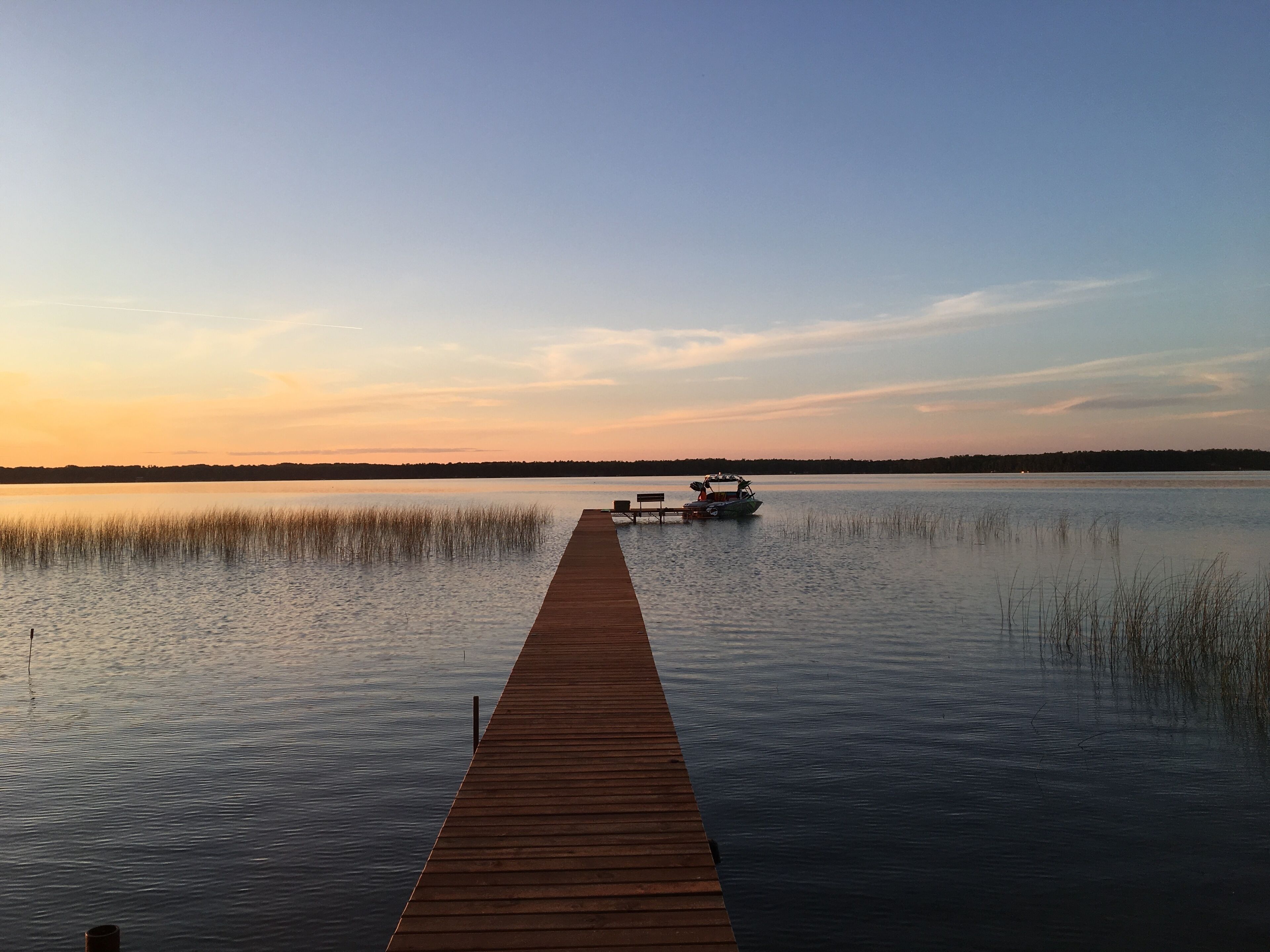 A wooden pier extending into calm water with a boat docked at the end.