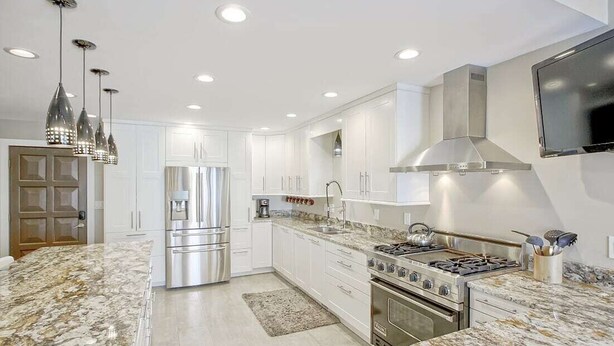 Una cocina moderna con armarios blancos, electrodomésticos de acero inoxidable, encimeras de granito e iluminación colgante.