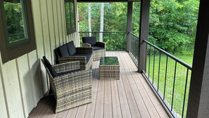 Un porche cubierto con muebles de mimbre y vistas a un área boscosa.
