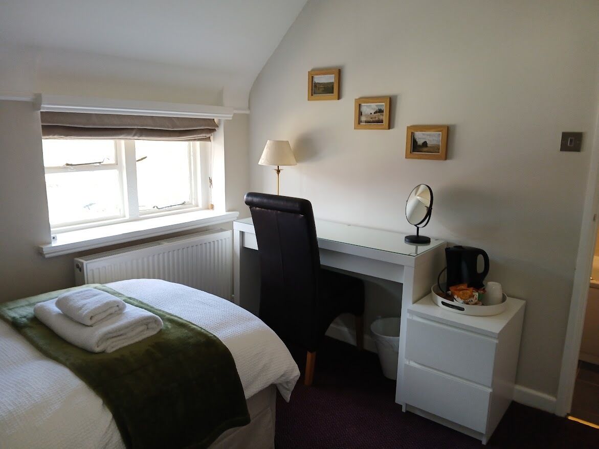 A hotel room with a bed, a desk, a chair, a lamp, a coffee maker, and a small table with a cup and saucer.