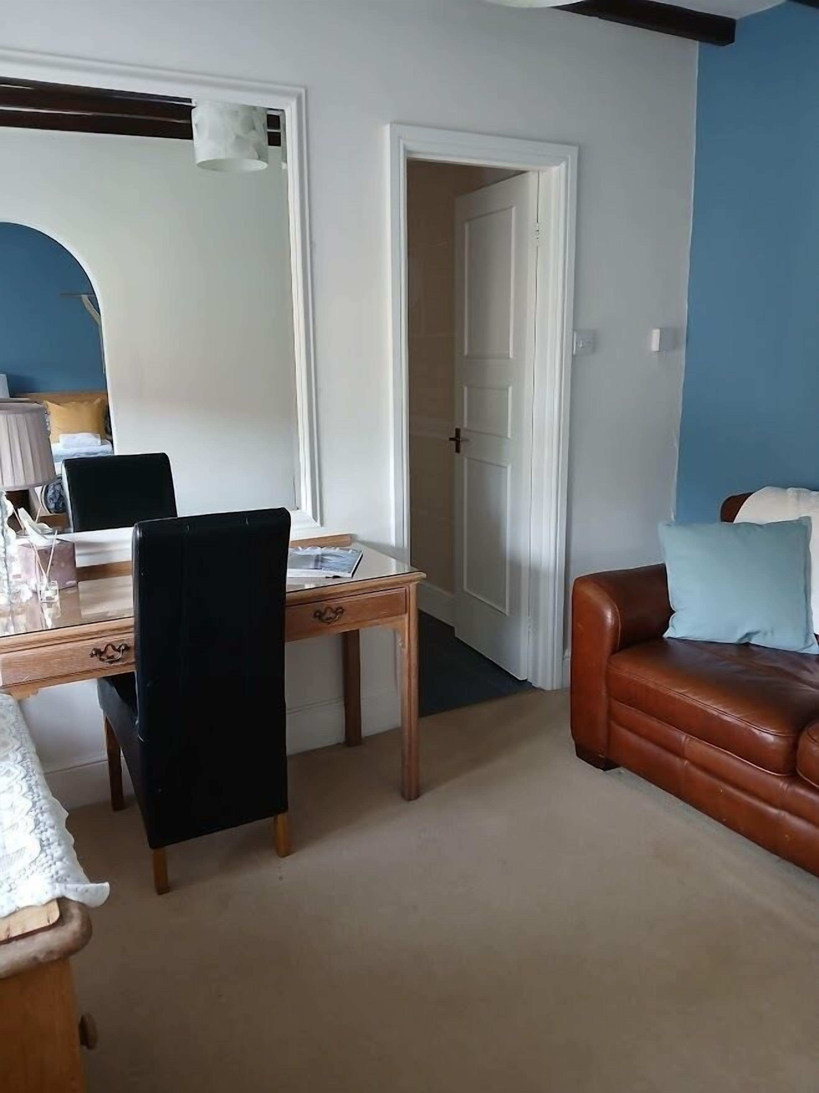 A room with a desk, chair, leather sofa, and a door leading to another room.
