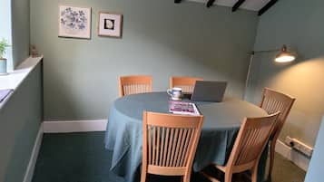 A room with a round table, four wooden chairs, a laptop, a lamp, and two framed pictures on the wall.