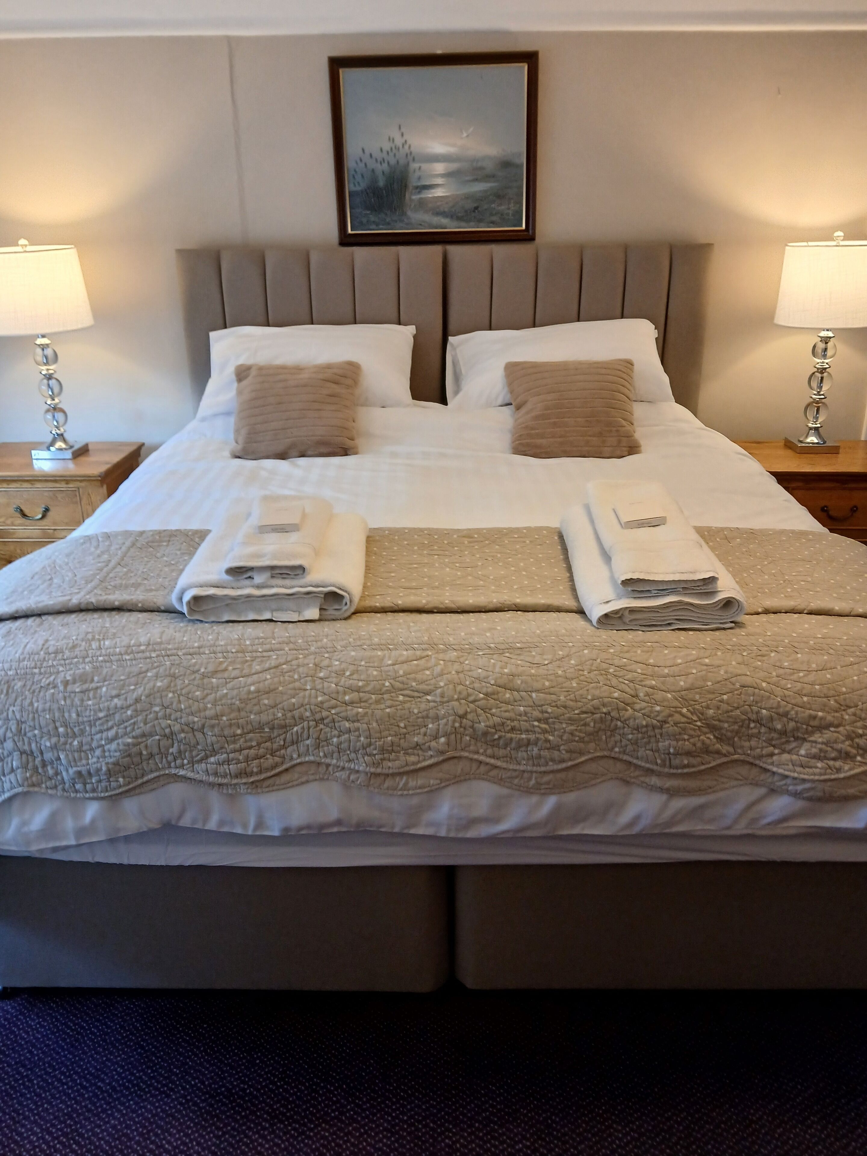A neatly made bed with two pillows, a quilt, and two folded towels.