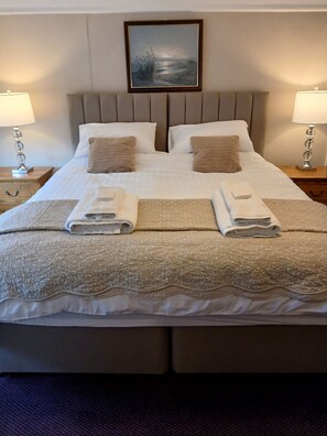 Una cama bien hecha con dos almohadas, un edredón y dos toallas dobladas.