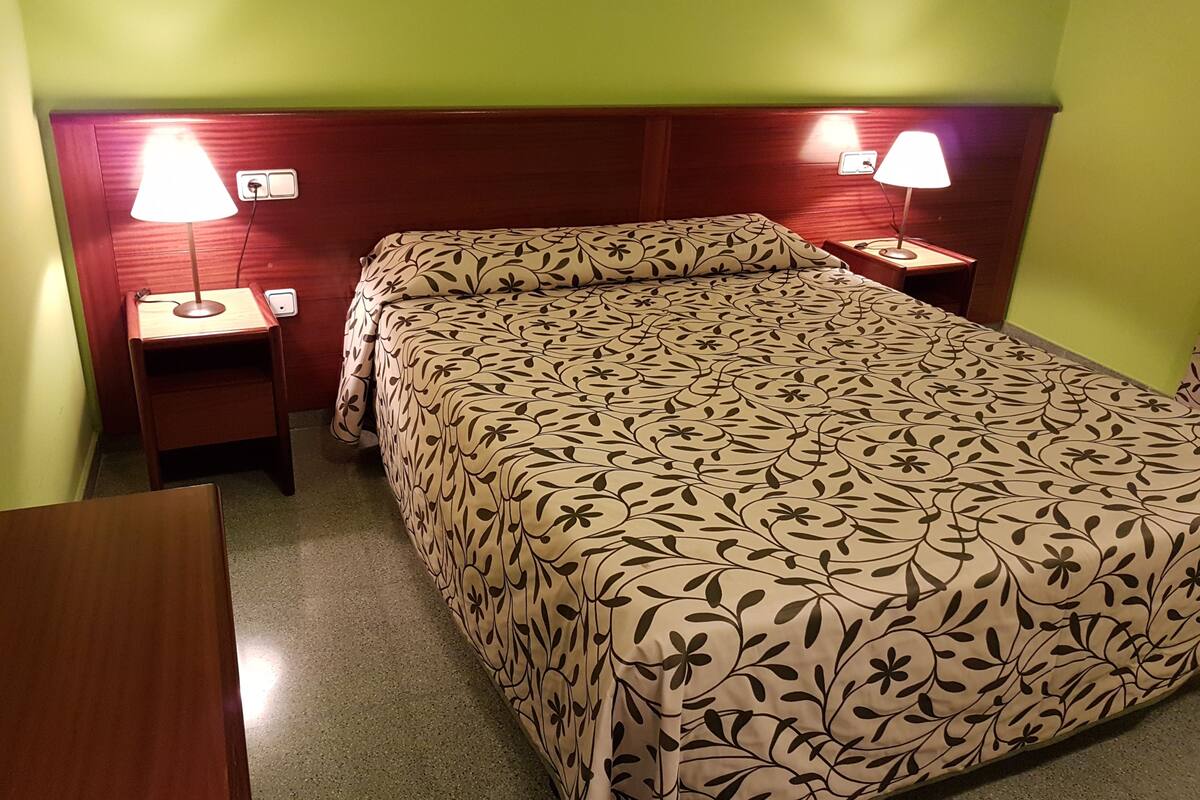 Une chambre d’hôtel avec un lit, deux tables de chevet et deux lampes fixées au mur.