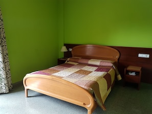 A single bed with a wooden frame, a quilt, a nightstand with a lamp, and a power outlet on the wall. - Hotel Don Pelayo (L'Arboc)