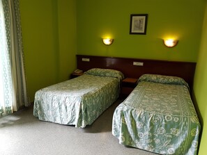 Une chambre avec deux lits simples, des murs verts et deux appliques murales.